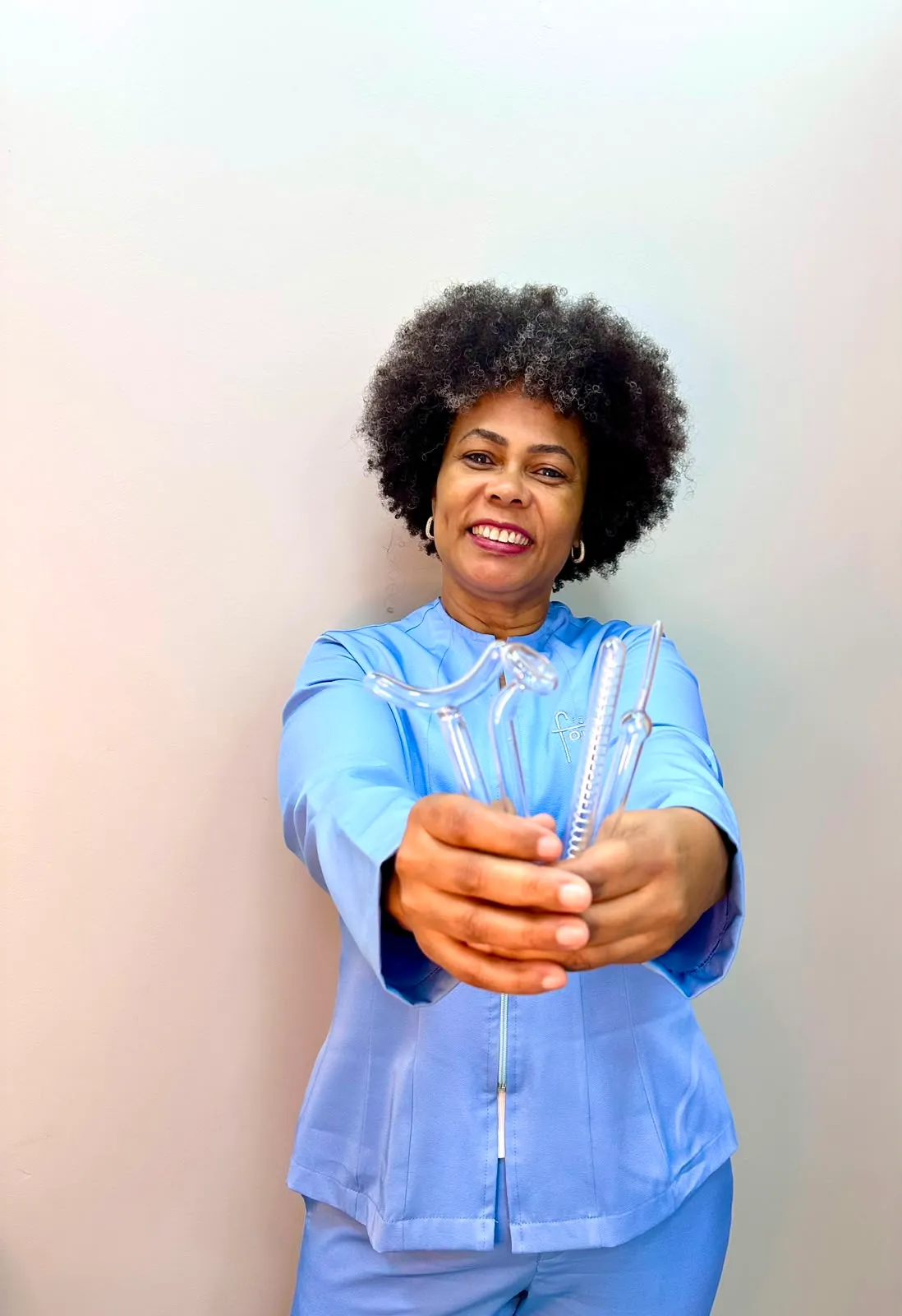 Célia Medina, esteticista, de jaleco azul claro do Espaço Forma Viva, segurando os eletrodos de alta frequência