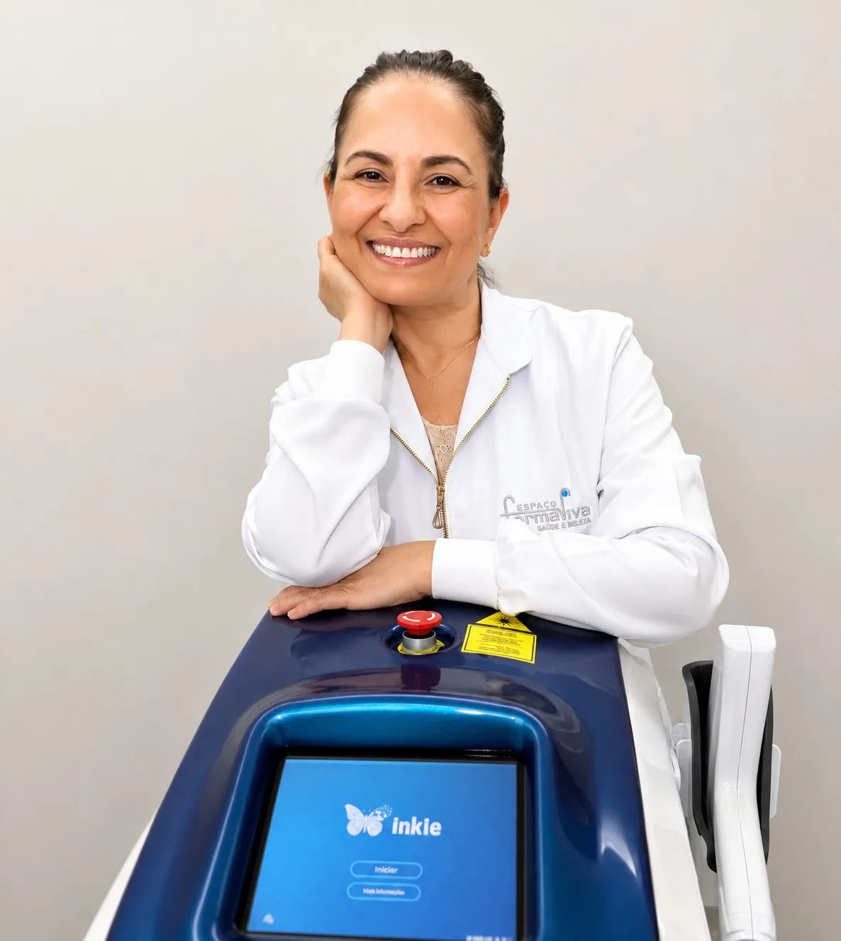 Marisabel Henrique, podóloga responsável, de jaleco branco com o logo do Espaço Forma Viva, ao lado do aparelho de laser da clínica